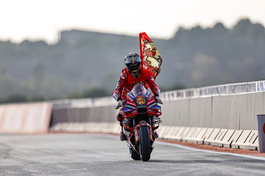 Un pilote de MotoGP en tenue rouge, sur sa moto, tenant un drapeau en célébration sur la piste lors de la course.