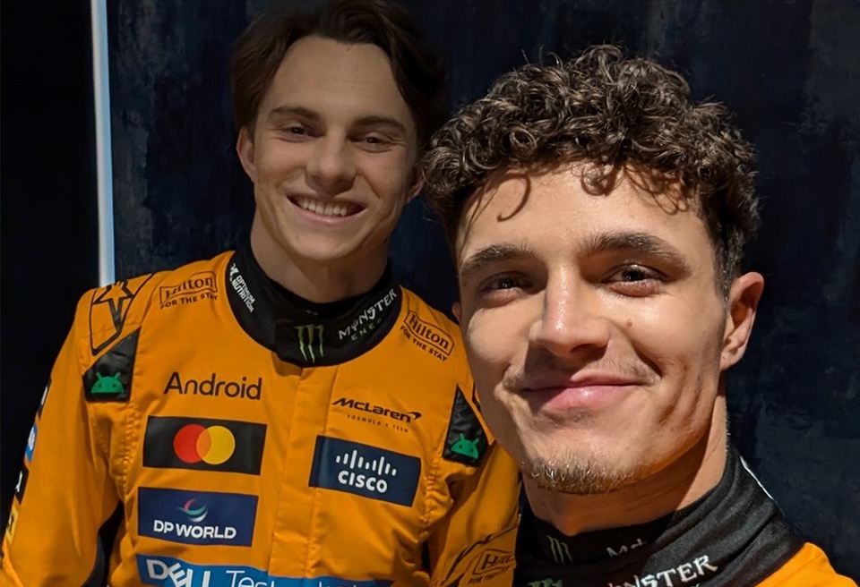 Deux pilotes de Formule 1 souriant ensemble, habillés en combinaison de course McLaren, posent pour un selfie.