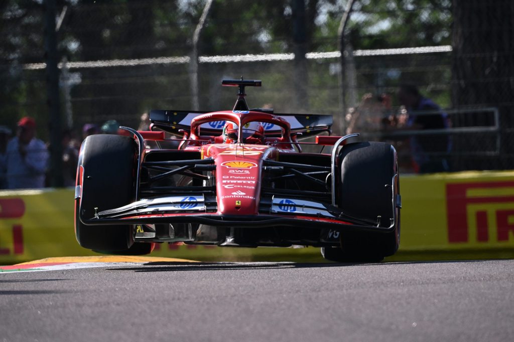 Une voiture de Formule 1 de l'équipe Ferrari prenant un virage en surélevant ses roues arrière sur le circuit d'Imola, avec des spectateurs en arrière-plan.