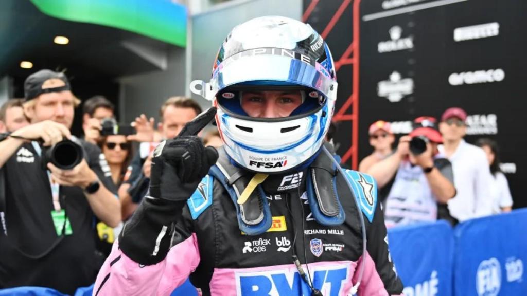 Victor Martins, pilote de Formule 2, célébrant son moment avec un doigt pointé vers le haut, entouré de fans et de médias lors d'un événement de course.