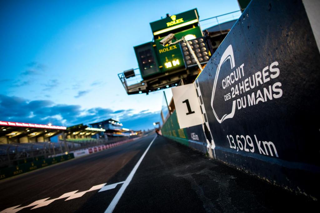 Vue du circuit des 24 Heures du Mans avec le panneau d'arrivée et le chronomètre en arrière-plan, à l'aube.