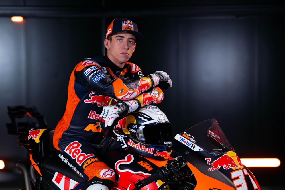 Portrait de Pedro Acosta, jeune pilote de MotoGP, assis sur sa moto Red Bull KTM, avec un regard déterminé et vêtu de son équipement de course.