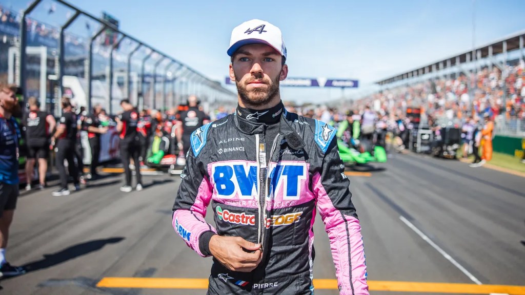 Pierre Gasly, pilote de l'équipe Alpine, en combinaison de course sur la grille de départ, avec des voitures et des membres d'équipe en arrière-plan lors d'un événement de Formule 1.
