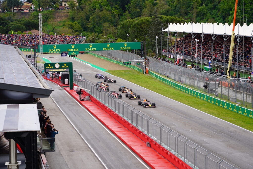 Vue panoramique de la course sur le circuit d'Imola lors du Grand Prix d'Émilie-Romagne 2025, avec plusieurs voitures de Formule 1 en action sur la piste et des spectateurs en arrière-plan.