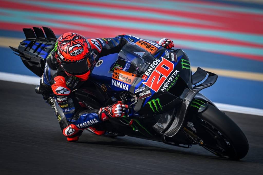 Un pilote de motocyclette en train de prendre un virage sur une piste de course, affichant des couleurs vives de l'équipe Yamaha et sponsorisé par Monster Energy.