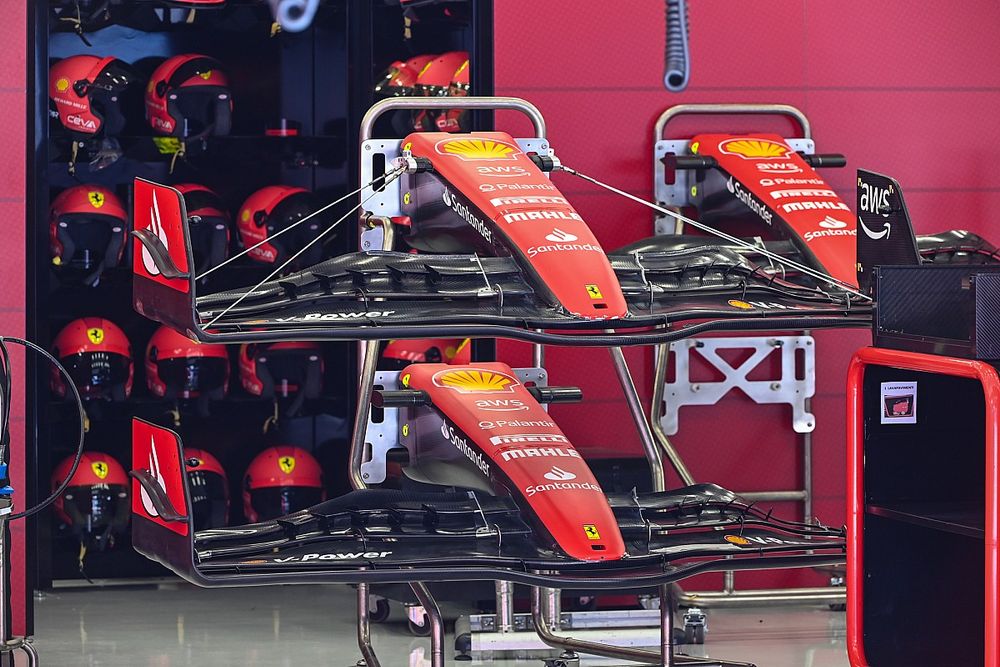Deux ailerons avant de Formule 1 Ferrari SF-25 dans le garage, avec des casques rouges en arrière-plan.