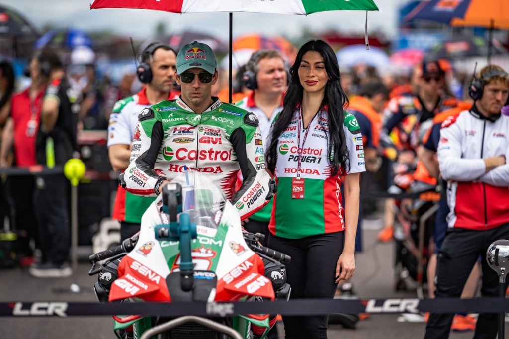 Johann Zarco, pilote de MotoGP chez LCR Honda, se prépare sur la grille de départ avec une équipe encadrante, tenant une ombrelle pendant que la moto est mise en place.