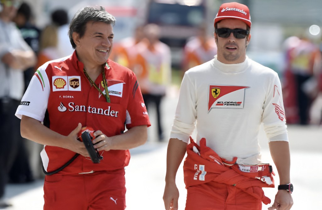 Fabrizio Borra et Fernando Alonso marchant ensemble dans un paddock de Formule 1, tous deux vĂȘtus de vĂȘtements de l'Ă©quipe Ferrari.
