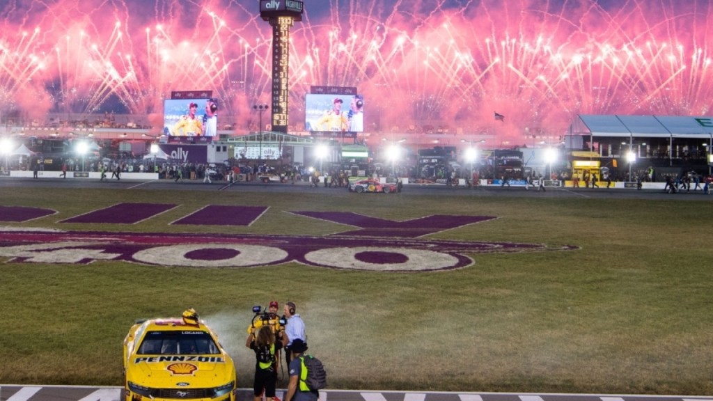 Fireworks illuminate the night sky above the Nashville Superspeedway with colorful bursts, while a NASCAR car is parked on the track, capturing a moment from the race event.