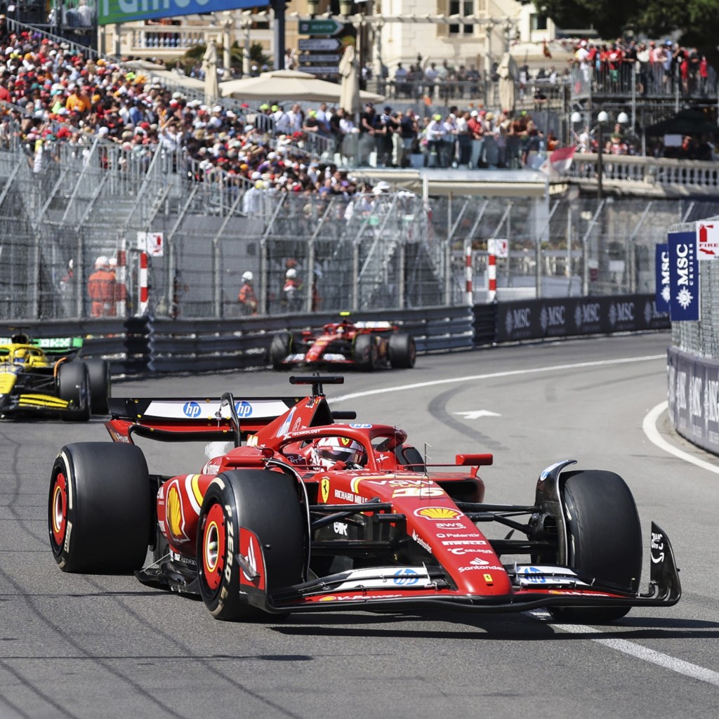 Une voiture de Formule 1 rouge, participant au Grand Prix de Monaco, prend un virage sur le circuit urbain, avec des spectateurs et des bâtiments historiques en arrière-plan.
