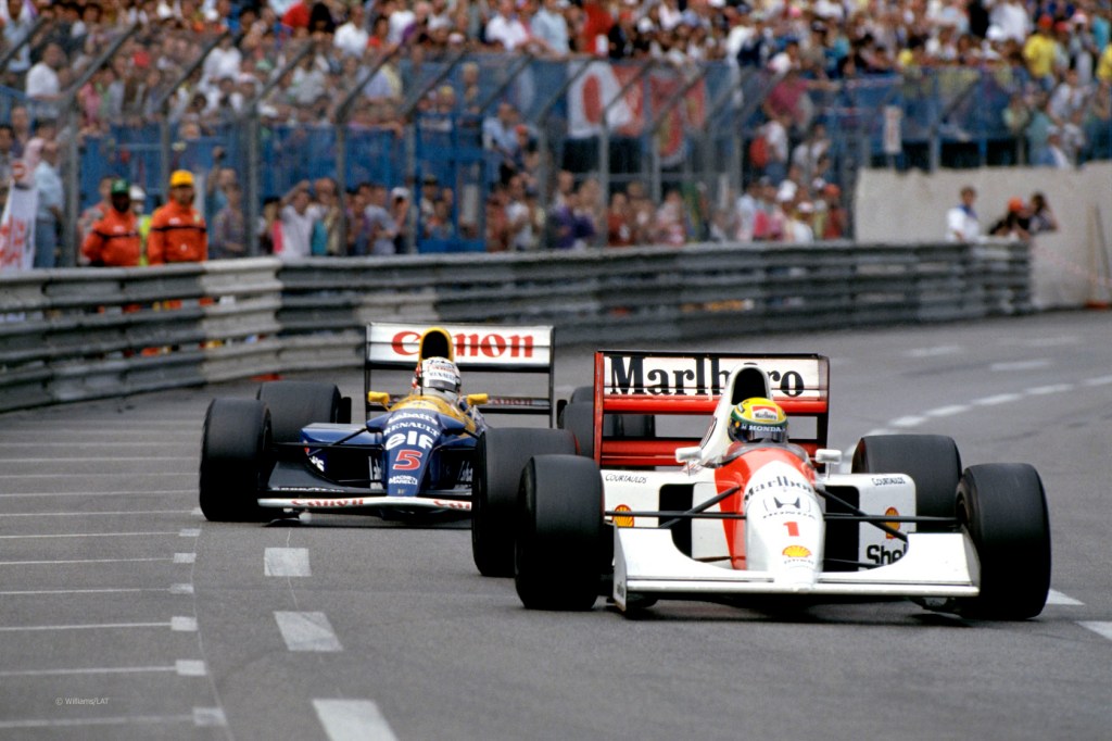 Ayrton Senna and Nigel Mansell racing closely in their iconic Formula 1 cars during the 1992 Monaco Grand Prix, with a crowd of spectators in the background.