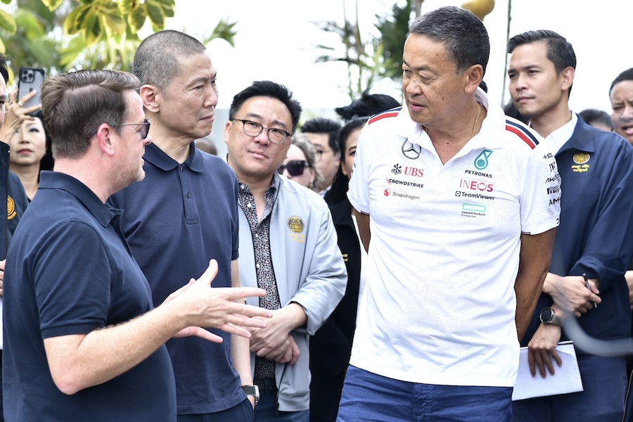 Group of men discussing plans for a Formula 1 event in Thailand, with one man wearing a Mercedes team shirt.