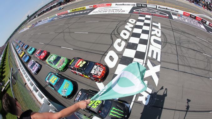 Vue aérienne des voitures de NASCAR franchissant la ligne d'arrivée à Pocono Raceway, avec un drapeau vert agité.