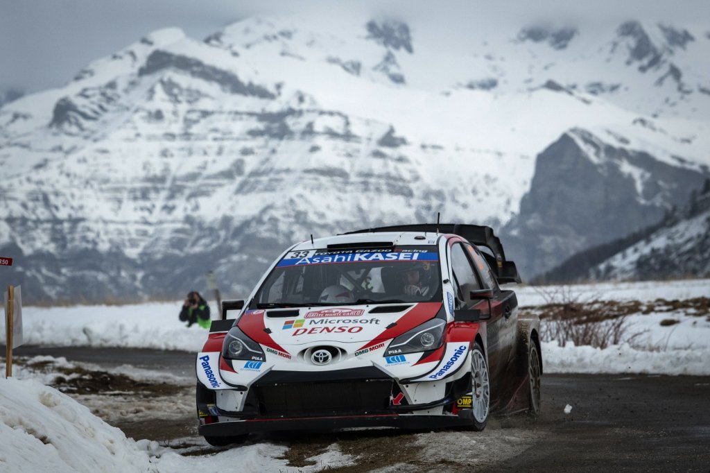 Voiture de rallye Toyota sur une route de montagne enneigée, avec des montagnes en arrière-plan.