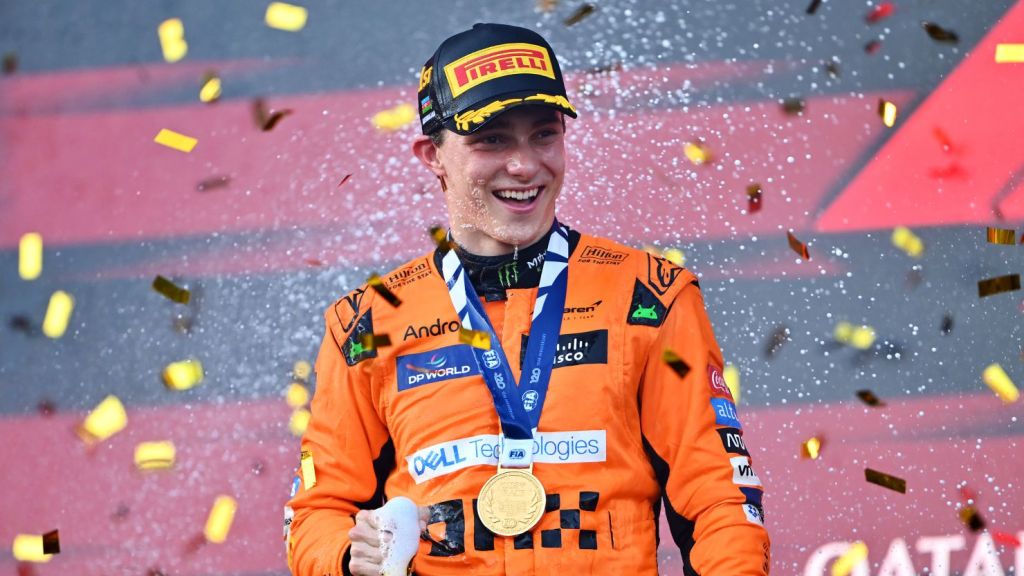 Pilote souriant en tenue de course McLaren, célébrant sa victoire avec une médaille et des confettis dorés autour de lui.