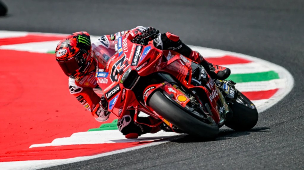 Un pilote de MotoGP en pleine action sur sa moto Ducati, en train de prendre un virage sur une piste colorée.