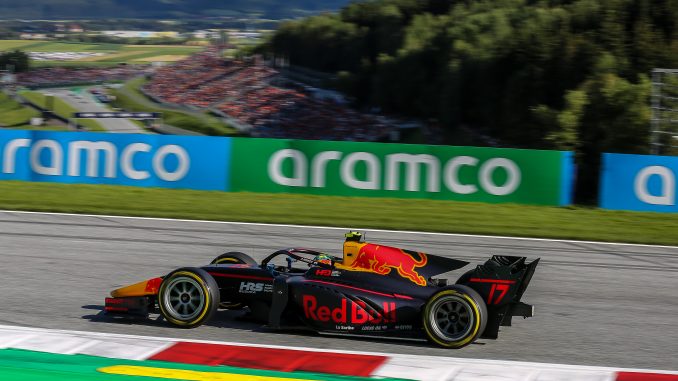 Une voiture de course aux couleurs de Red Bull passe sur le circuit Red Bull Ring, avec des spectateurs en arrière-plan.
